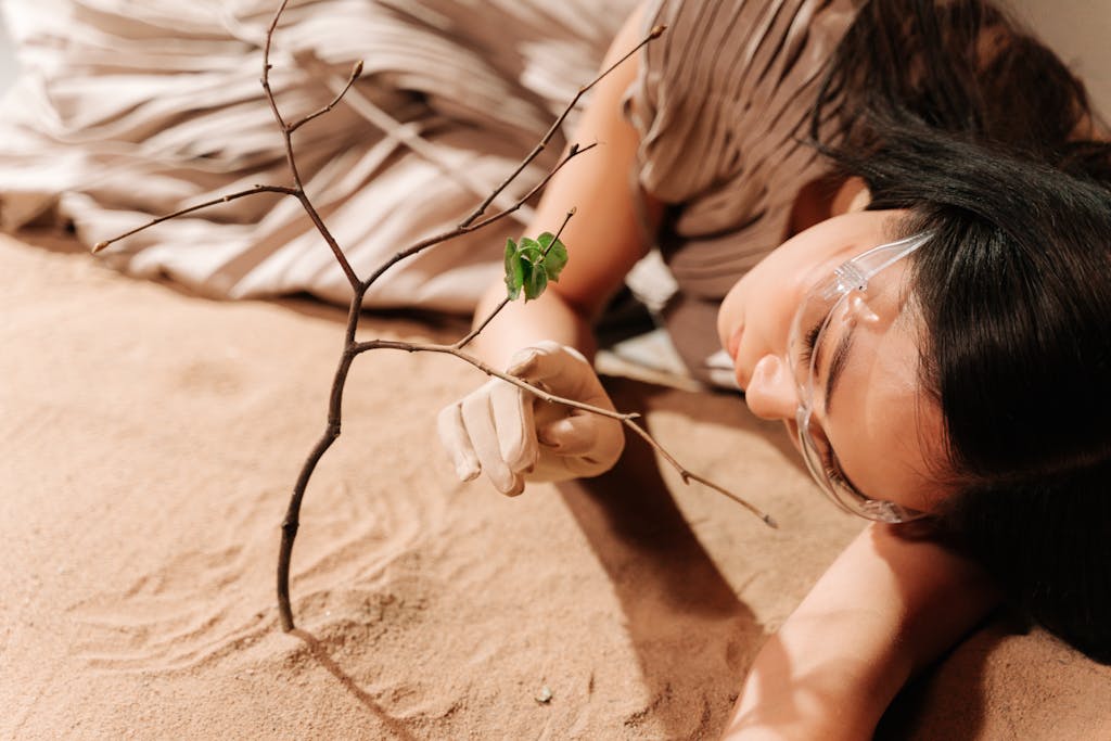 A woman lies on sandy ground grasping a small branch, symbolizing hope in arid conditions.