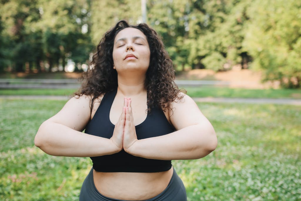 A woman practicing meditation in a park, focusing on wellness and fitness outdoors.