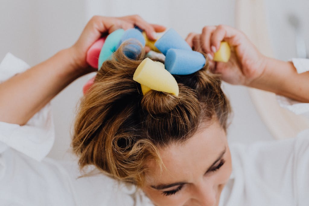 Close-up of a woman using colorful foam rollers to style her hair indoors.