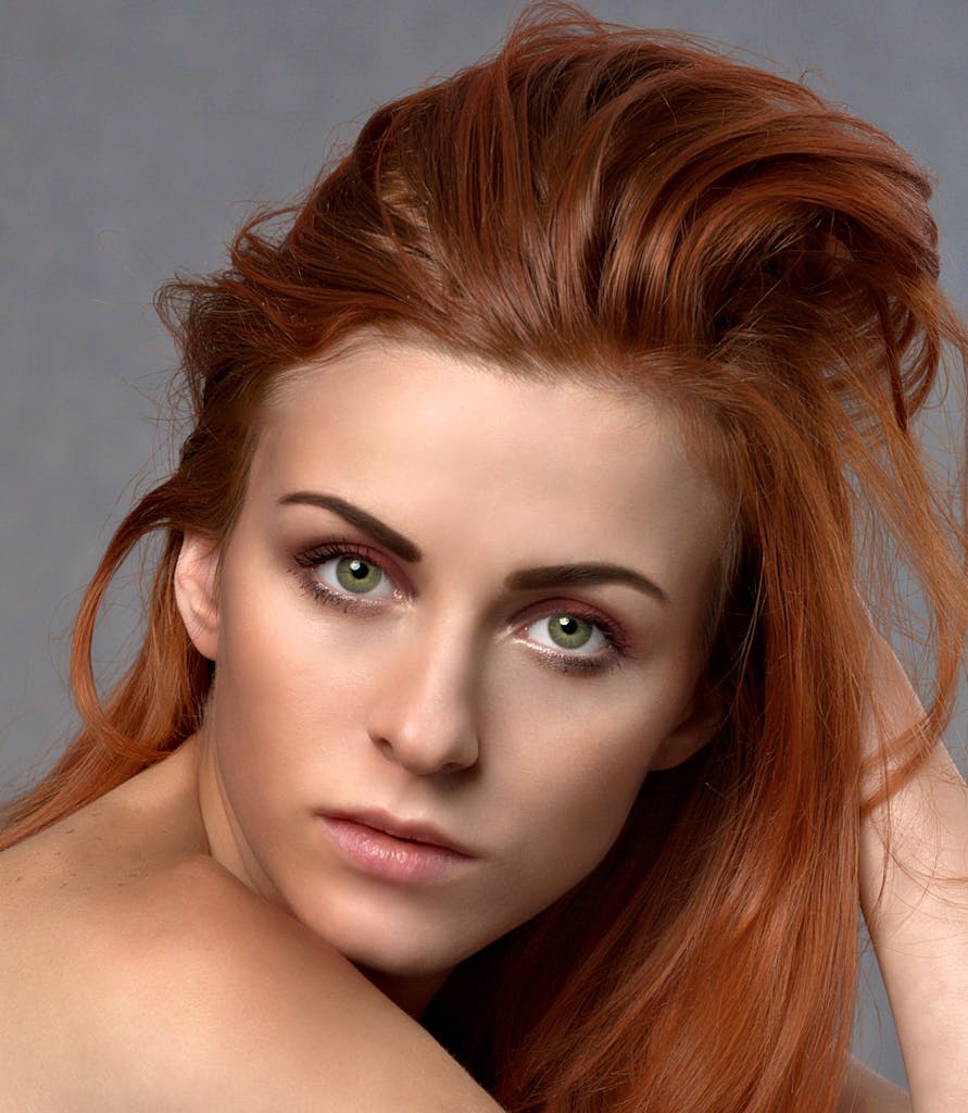 Close-up portrait of a woman with striking red hair and green eyes, exuding elegance.