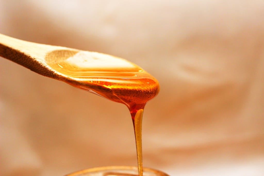 Macro shot of golden honey pouring from a wooden spoon, emphasizing its rich texture and color.