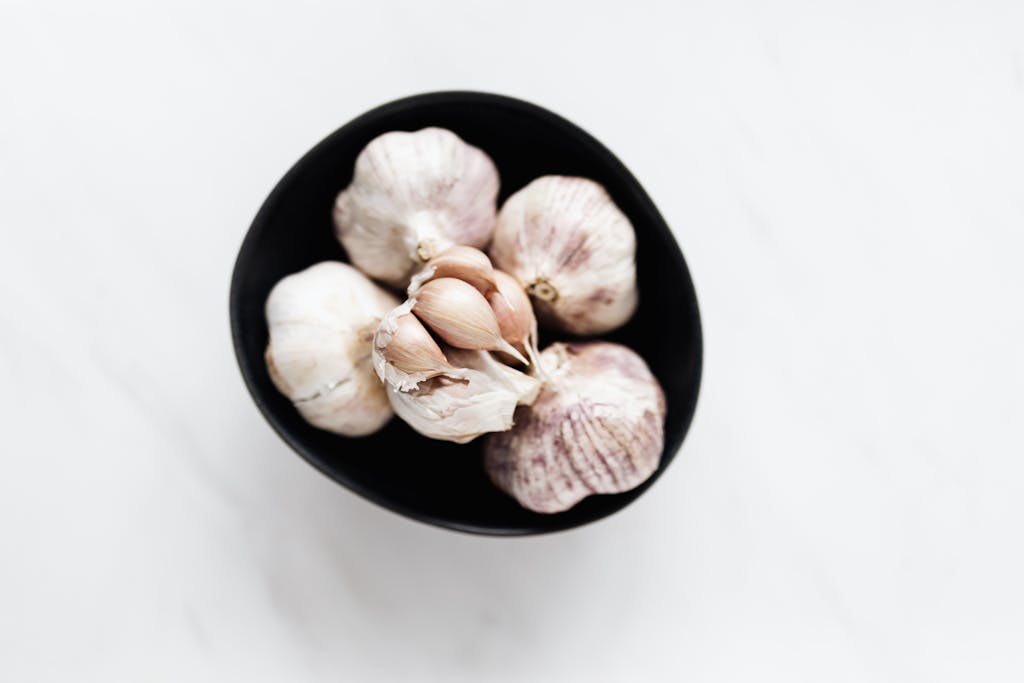 Overhead view of fresh garlic bulbs in a black bowl on a marble surface highlighting culinary freshness.