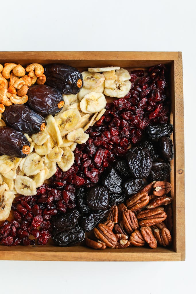 Top view of a wooden tray filled with assorted dried fruits and nuts, offering a healthy snack.